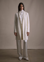 Image of a model standing forwards wearing ivory long sleeved coat, over ivory charmeuse top and pant.s