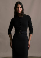 Model wearing a black long sleeve cardigan with crystal flower buttons over a lace shirt with a black belted skirt. 
