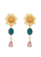 A flat lay of dangle earrings that include a gold flower and green and pink charms.