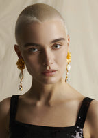 A model wearing earrings that have a large gold flower then a white stone the a crystal.