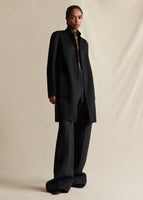 Model wearing a black mid length cashmere coat, styled with black wide leg pants.