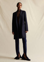 An image of a model wearing a navy blue mid length cashmere coat, with navy blue flare pants that have a high slit. Styled over a black lace turtleneck.