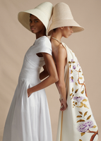 An image of two models standing back to back, one wearing the Sibyl Dress in Cotton Poplin and one wearing the Halter Dress in Printed Crepe.