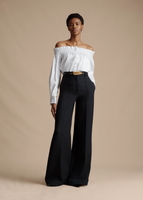 A model posing while wearing the Visby Top in Cotton Poplin, paired with the Deeda Pant in Silk Wool and Fern Belt.