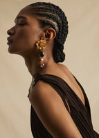 A model wearing gold flower earrings with a green stone and crystal drop down.