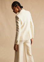 Image of a model standing backwards wearing an ivory long sleeved blazer with ivory pants.