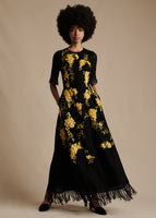 Model is wearing the embroidered Eloise Dress in Lino Weave. The dress is ankle length with a black bodice and yellow embroidered flowers.