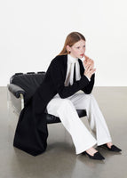 Model sitting on a chair wearing the vanessa coat in zibeline cashmere in black