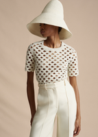 A model wearing the Embroidered Top in Pearl Lattice, paired with the Taiko Hat and the Deeda Pant in Silk Wool.