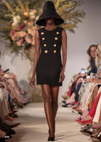 Model is facing forward wearing a classic Adam Lippes black sheath dress, updated with decorative gold flower buttons.