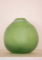 A round green glass vase on a pale pink background. 