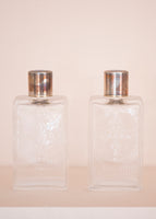 Matching glass perfume bottles with blue enamel tops on a pale pink background. 