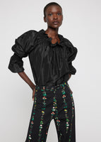 A model wearing a black taffeta top tucked into floral pants.