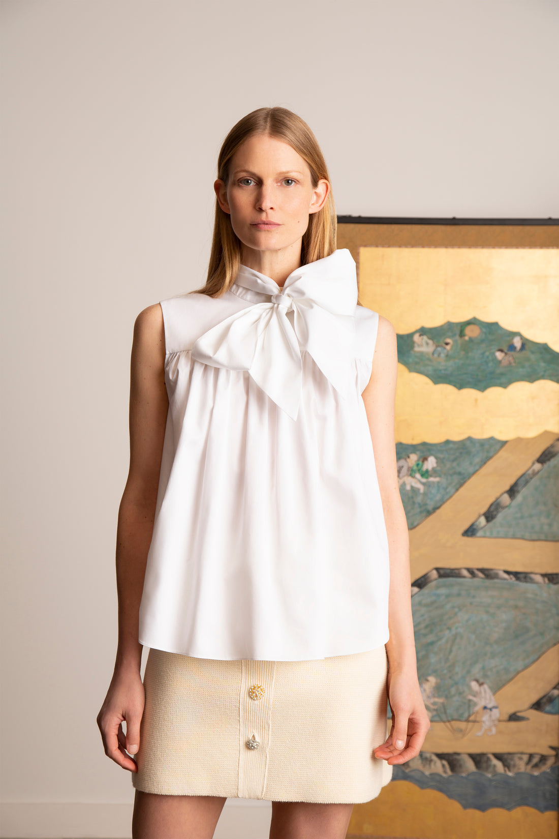 a model wearing a big bow neck shirt with a cream mini skirt 