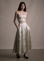 Model wearing a flare long skirt in champagne jacquard with floral details worn with matching set top. 