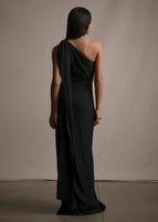 A back-facing image of a model wearing a floor length black satin one shoulder gown with wrap ribbon detail.