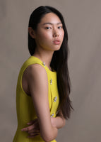 Image of a model from the waist up wearing a yellow sleeveless dress with silver crystal buttons.