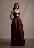 Model wearing a floor length fit and flare merlot gown with thin straps and gathered bow-like on front torso.