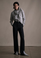 Model wearing long sleeve blouse with high neckline in stripe shirting with a tied bow at the front neck worn with black pants.