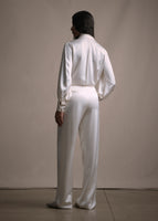 A back-facing image of a model wearing long straight leg double-pleat pant in ivory with matching blouse. 