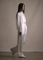 Side-angle image of model wearing long straight leg double-pleat pant in ivory with matching blouse.