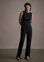 Model wearing a cropped sleeveless black gilet top with six buttons on the front paired with matching black pants. 