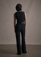 A back-facing shot of a model wearing long black pant and matching gilet.
