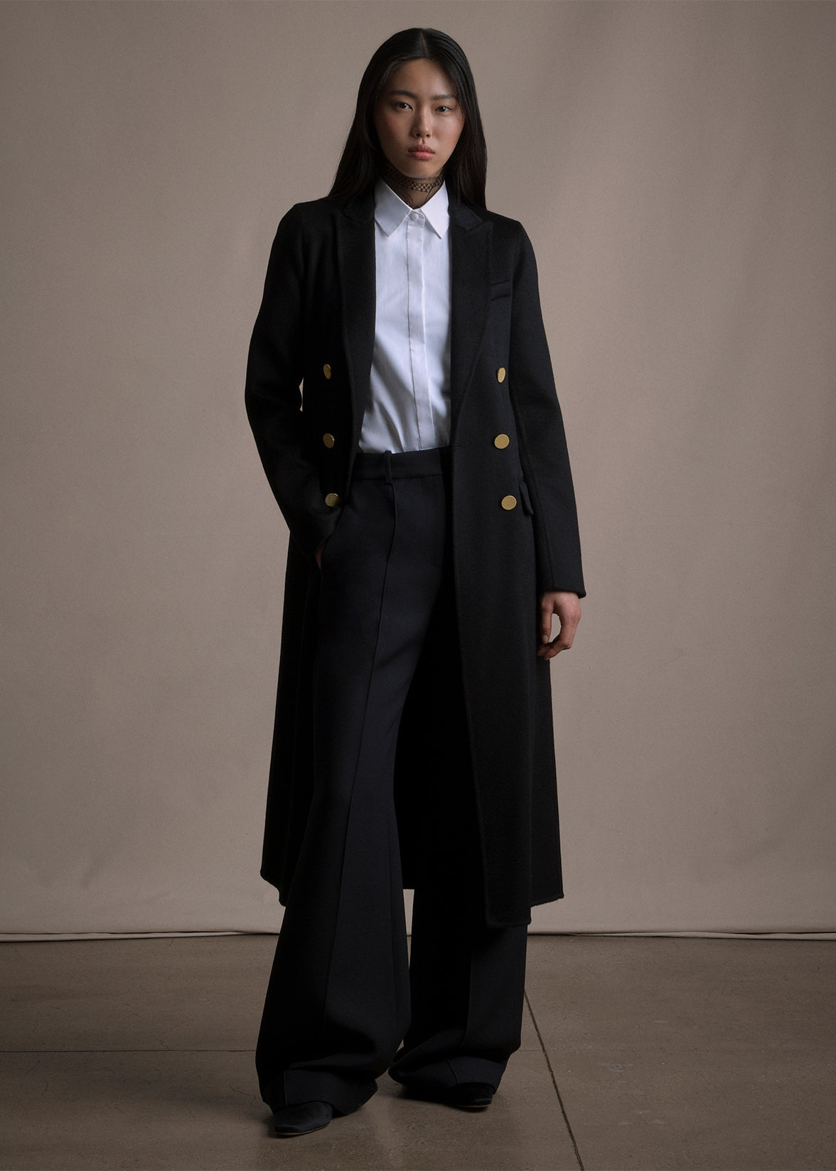 An image of a model wearing a black double breasted cashmere long coat over a white button down and black pants by Adam Lippes