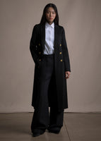 An image of a model wearing a black double breasted cashmere long coat over a white button down and black pants. 