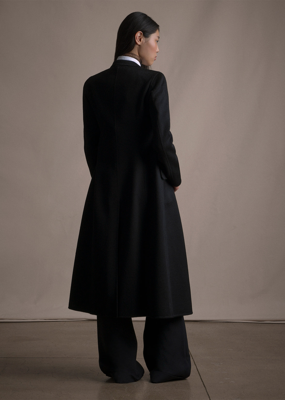 An image of a model standing backwards wearing a black long coat by Adam Lippes