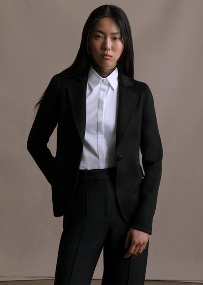 Image of a model facing forwards wearing black blazer over white button down shirt by Adam Lippes