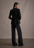 Image of a model standing backwards wearing a black blazer with black trousers.