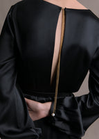 A zoomed in image of the back of a long sleeve black satin dress with a gold chain and pearl details.