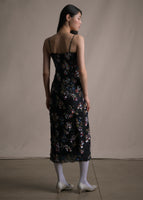 Image of a model facing backwards wearing a beaded floral black dress with thin straps.