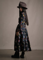 A back-facing image of model wearing floor length black sackville flare skirt with multicolor printed flowers and a matching top.