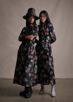Two models: The right wearing a matching top and skirt set in black floral with a hat. The left model wearing a long sleeve black floral mid length dress. 