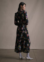 A back-facing image of model wearing a long sleeved black floral printed mid length dress.