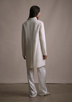 A model standing backwards wearing an ivory knee length coat over ivory pants.