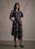 Model wearing a mid length black short sleeve asymmetrical dress with a tie front and multicolor printed flowers.