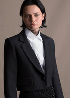 Image of a model from the waist up wearing a black cropped jacket over a white button down shirt.
