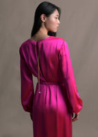 A zoomed in image of the back of a long sleeve pink satin dress with a gold chain and pearl details.