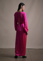 A back-facing image of a model wearing a long sleeve floor length pink satin dress tied with a gold chain and pearl detailing.