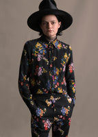 Model wearig black long sleeve shirt with collar, thin bow, and multicolor printed flowers with matching pants.