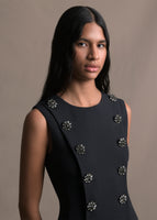 Image of a model wearing a black sleeveless sheath dress from the waist up with crystal buttons.