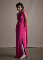 Side angle image of a model wearing a floor length hot pink satin one shoulder gown with a wrap ribbon detail.