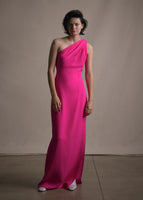 Model wearing floor length hot pink satin one shoulder gown with wrap ribbon detail.