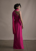 A back-facing image of a model wearing a floor length hot pink satin one shoulder gown with wrap ribbon detail. 