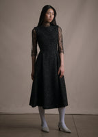 Model wearing a lace top under a black metallic fit flare dress. 