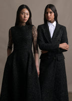 Two models the right wearing a lace top under a metallic fit and flare dress. The left model wearing a white top with a long black manteau. 