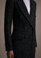 A zoomed in image of a white top under a log black manteau with buttons and two pockets.